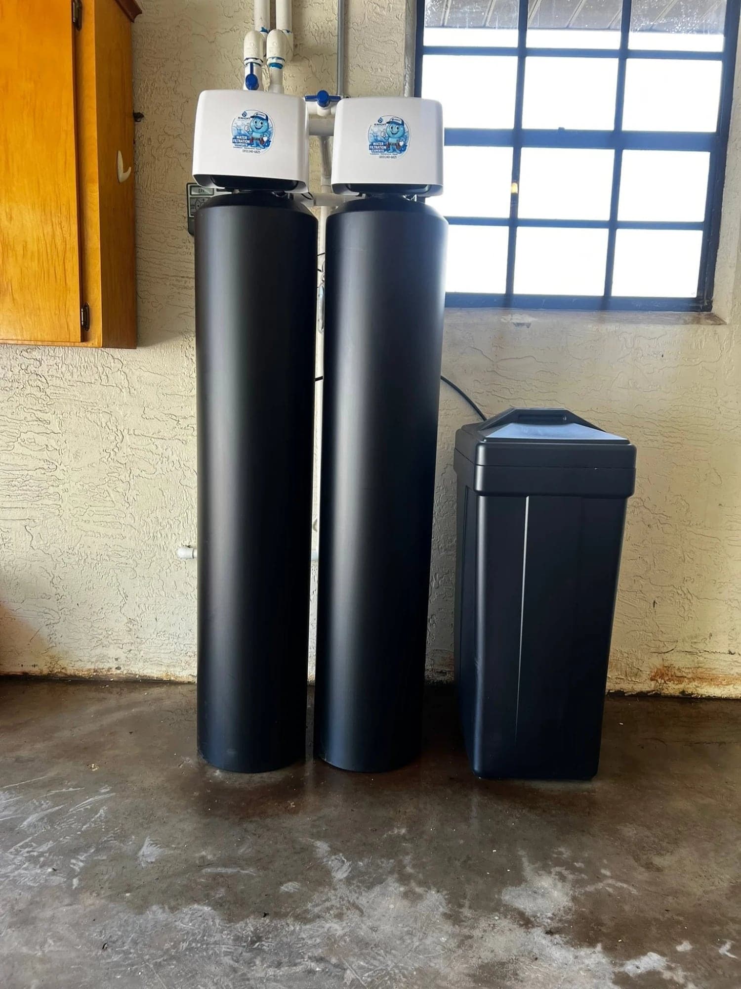 Two black water treatment tanks and a brine tank installed in a garage