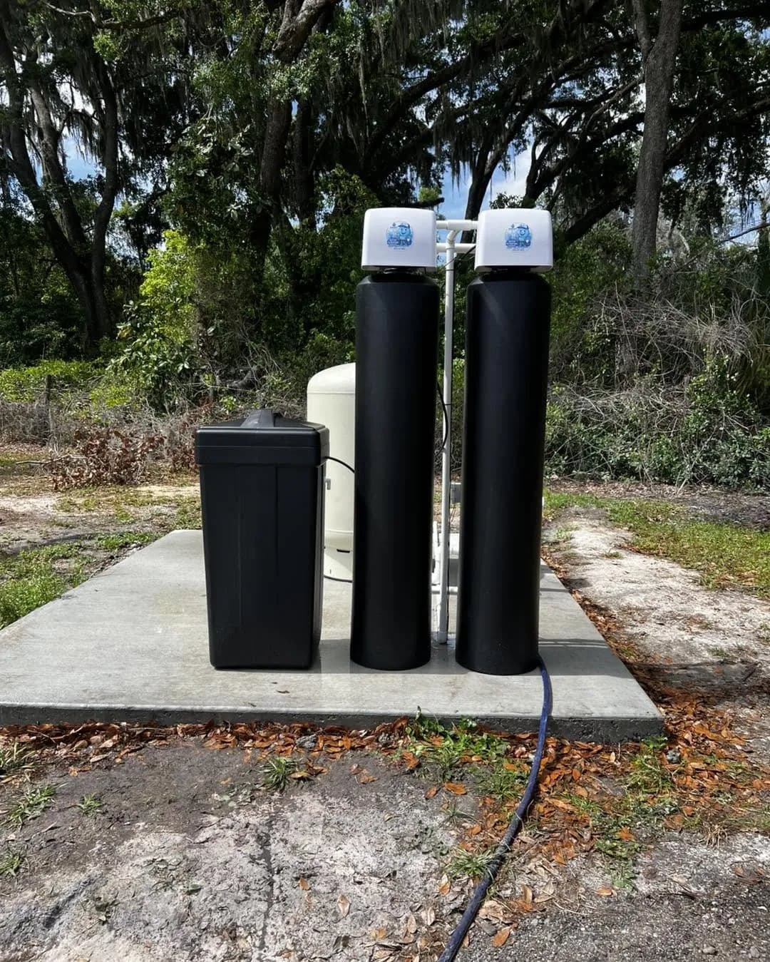 Two-tank water treatment system on a concrete pad under oak trees
